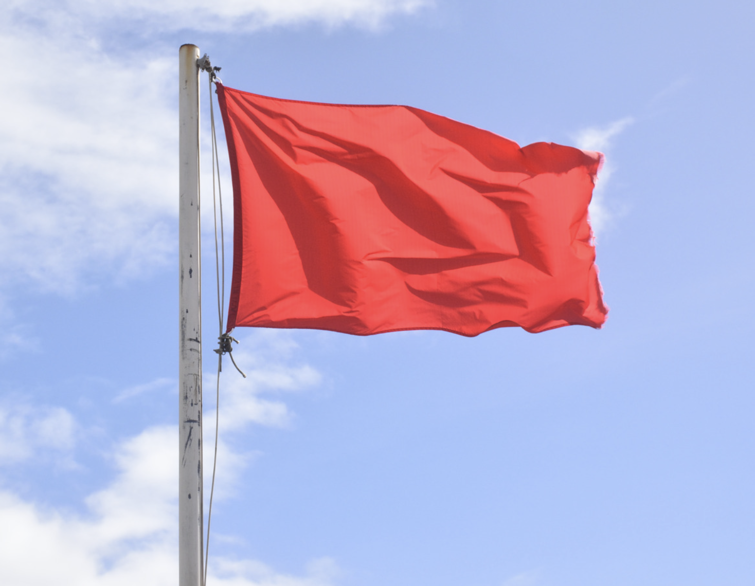 A red flag strung atop a flagpole on a sunny day