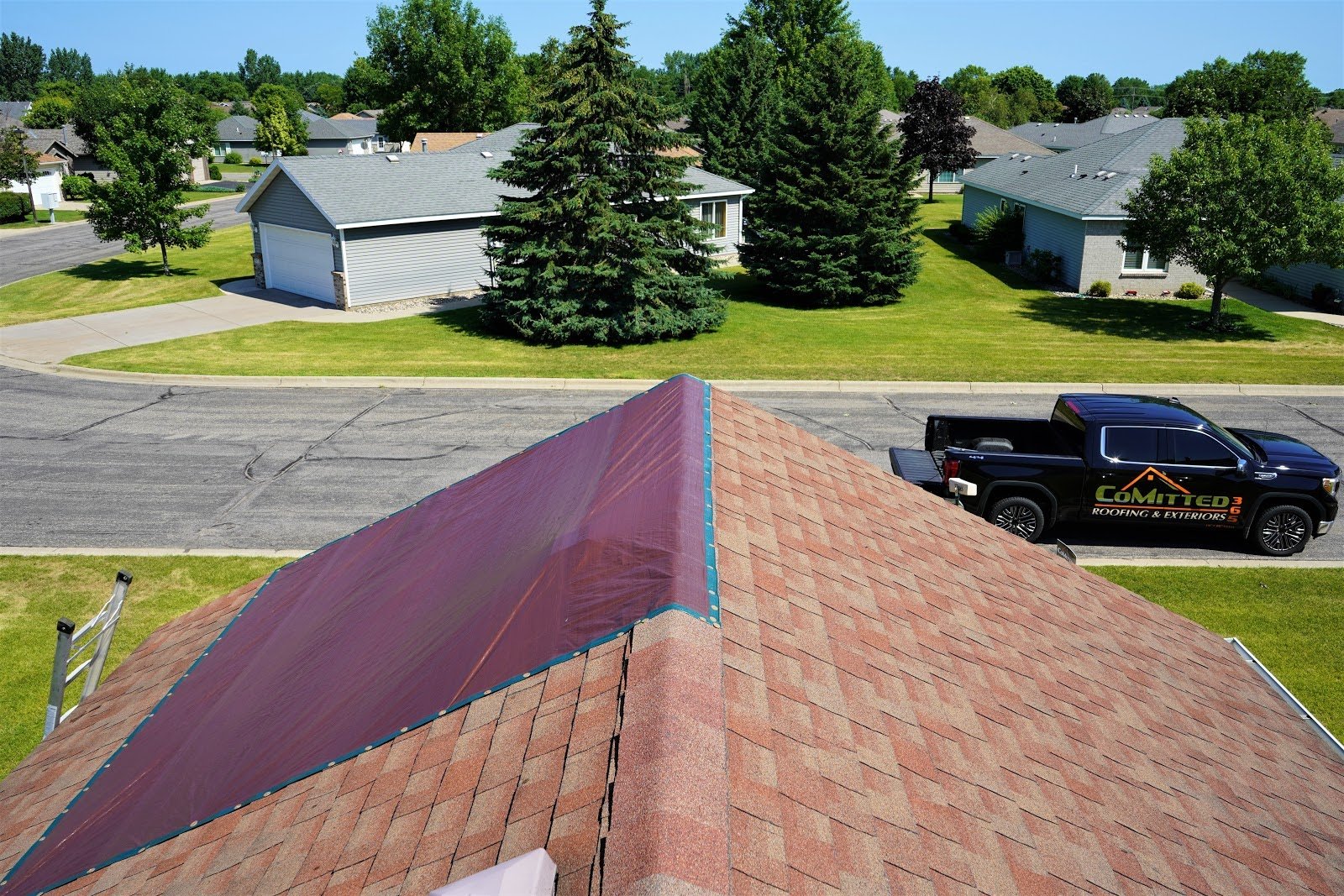A partially tarped roof on a home with a CoMitted 365 truck in front