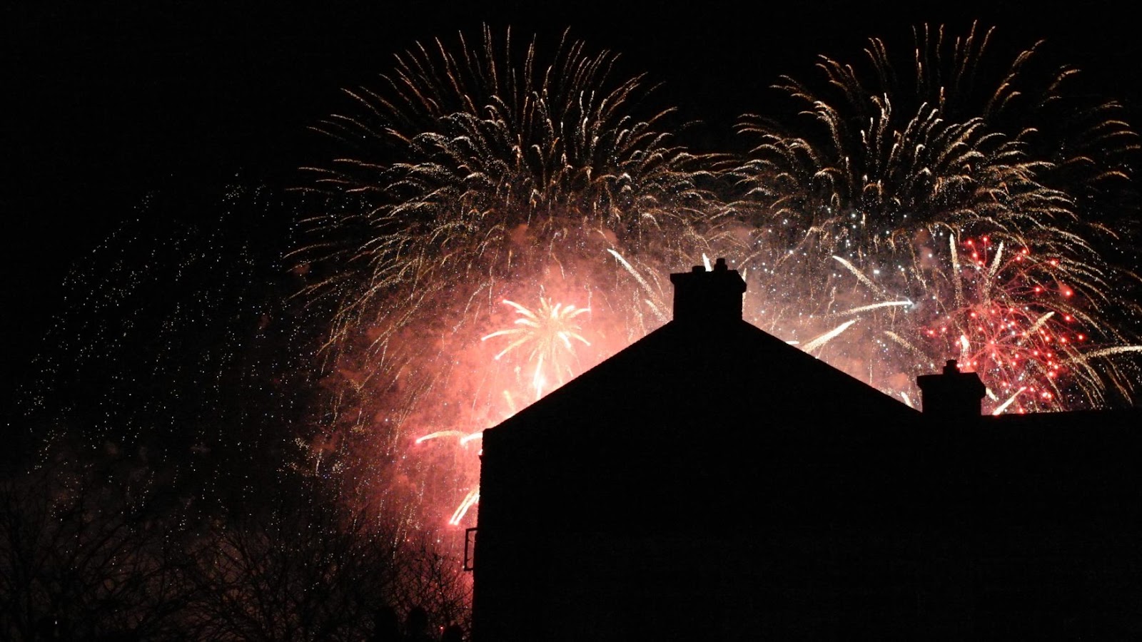 Fireworks exploding behind the silhouette of a home