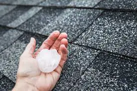 Hand holding a large hailstone near the roof shingles checking for hail damage in St Cloud 