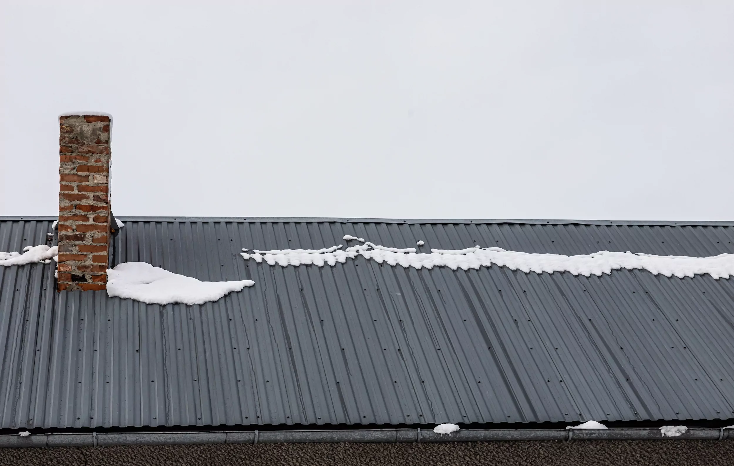 a brick chimney on a metal roof in the winter under the snow. construction concept.