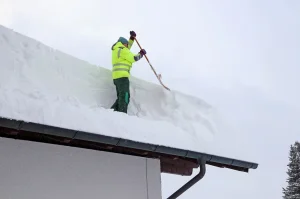 A man removing heavy snow from a roof to prevent structural damage in Minnesota